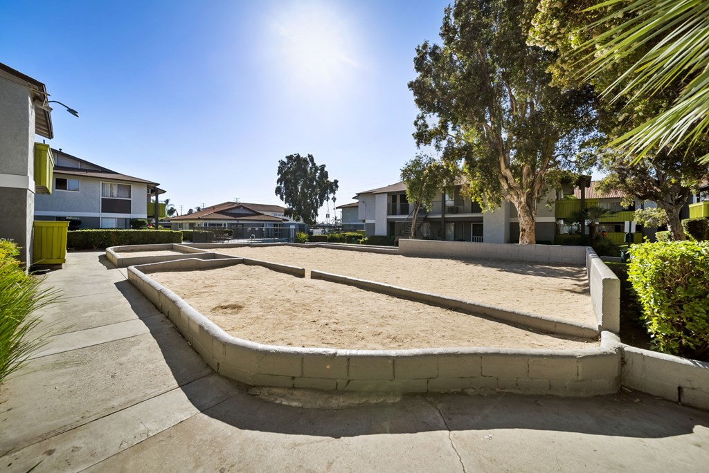 A sandbox in the middle of a concrete area with houses and trees in the background.