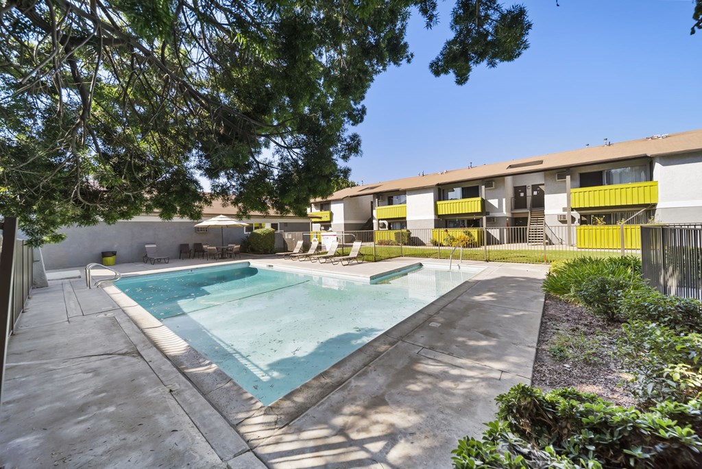 A swimming pool surrounded by trees and a building with yellow balconies.