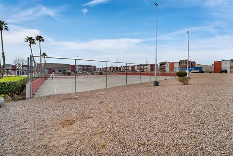 A gravel area with a fence and palm trees in the distance.