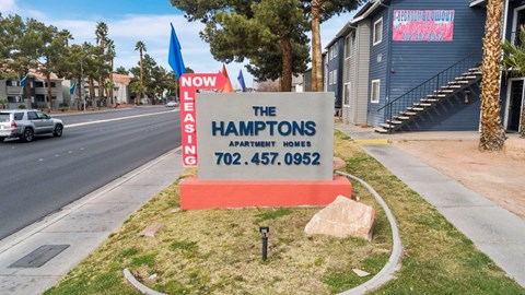 A sign for The Hamptons Apartment Homes is displayed in front of a building.