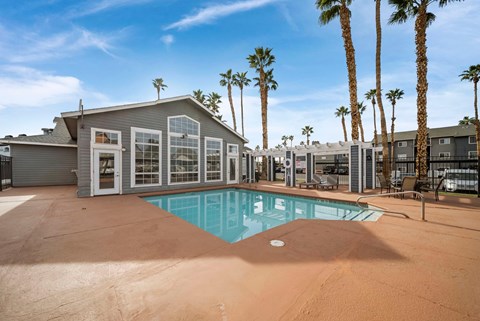 A pool surrounded by palm trees and a building with a patio.