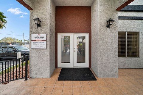 The entrance to a building with a sign that reads "Las Palomas" and a black doormat in front.
