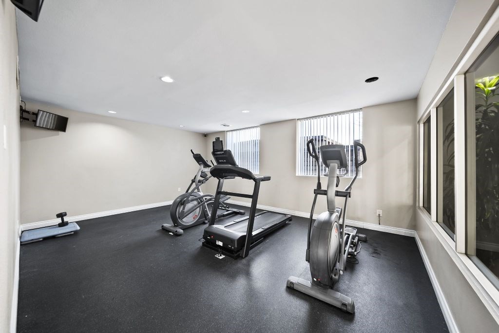 A room with a black floor and white walls has a row of exercise equipment.