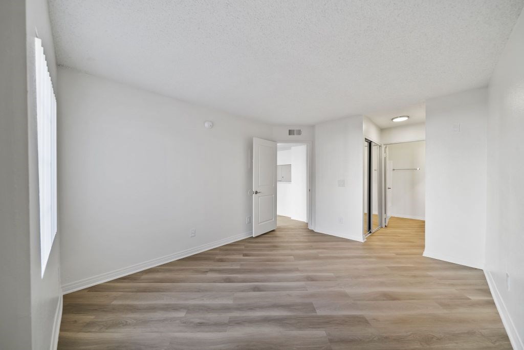 A long, empty hallway with wood flooring and white walls.