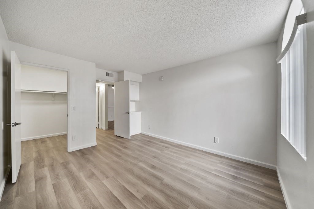 A spacious room with light wood flooring and white walls.