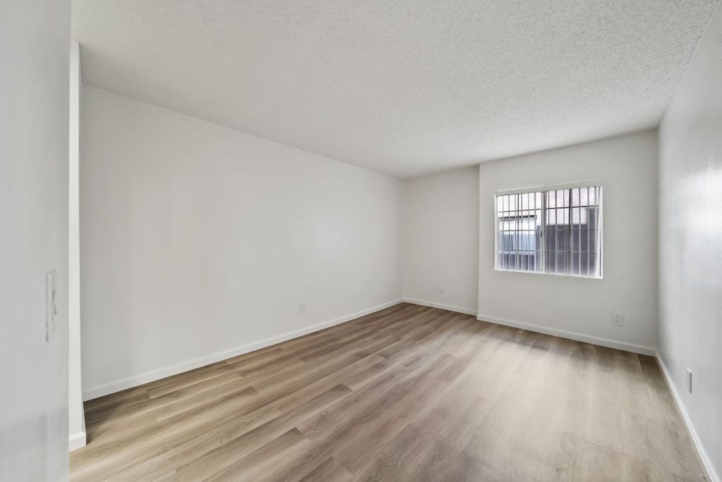 Empty room with wooden flooring and a window with bars.