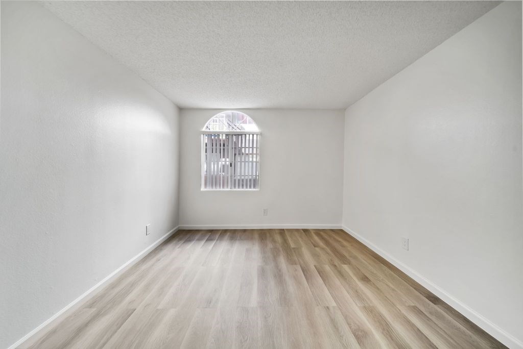A room with a wooden floor and a window with bars on it.