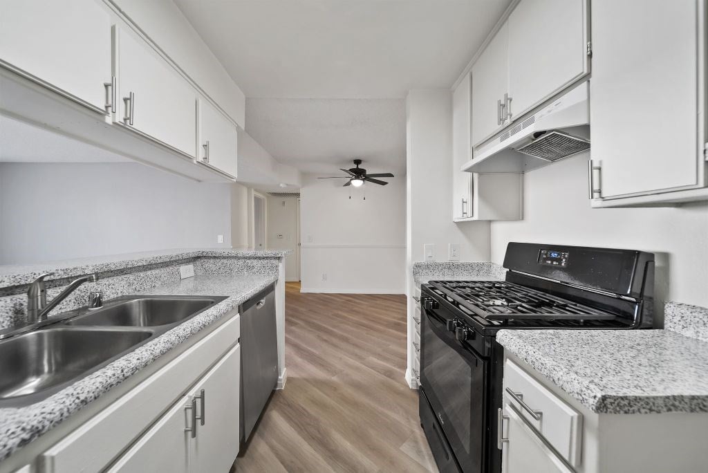 A kitchen with a black stove top oven and a sink with a granite counter top.