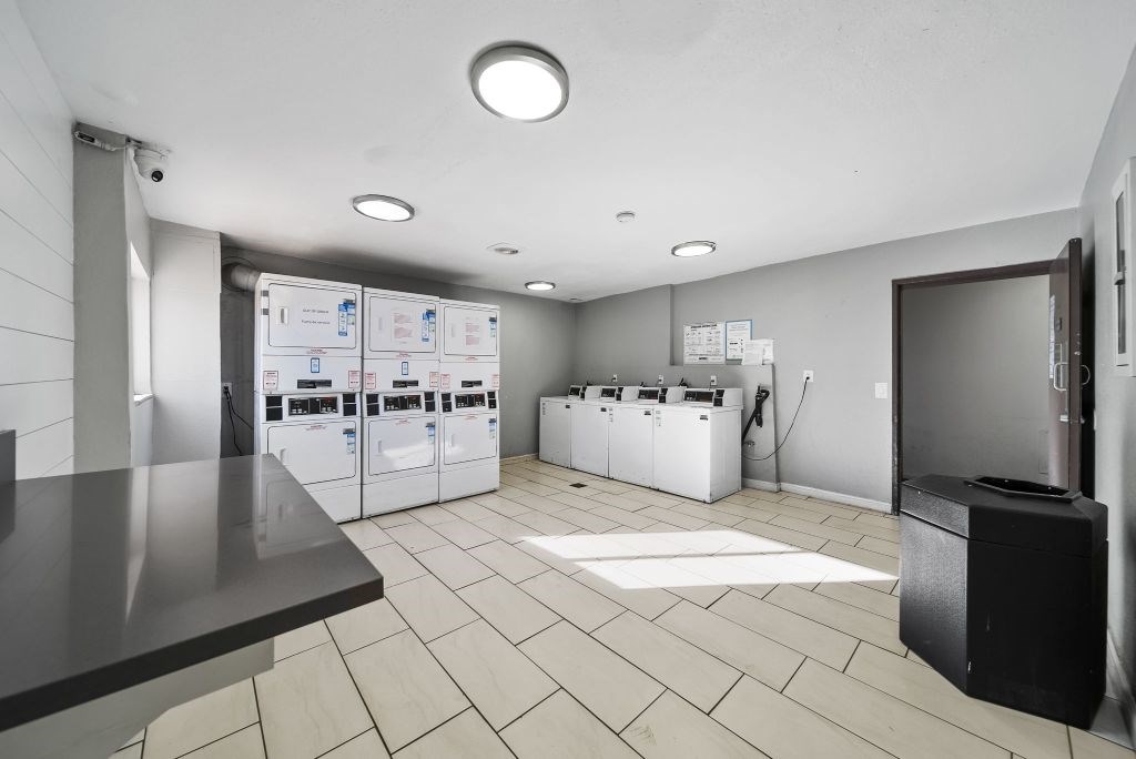 A clean, modern laundry room with a washer and dryer on the wall and a flat screen TV on the counter.