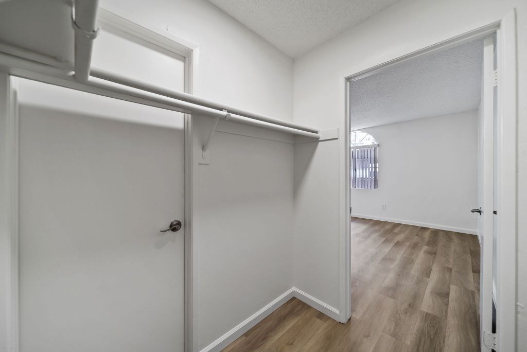 A white door with a black handle is in a room with white walls and wood flooring.