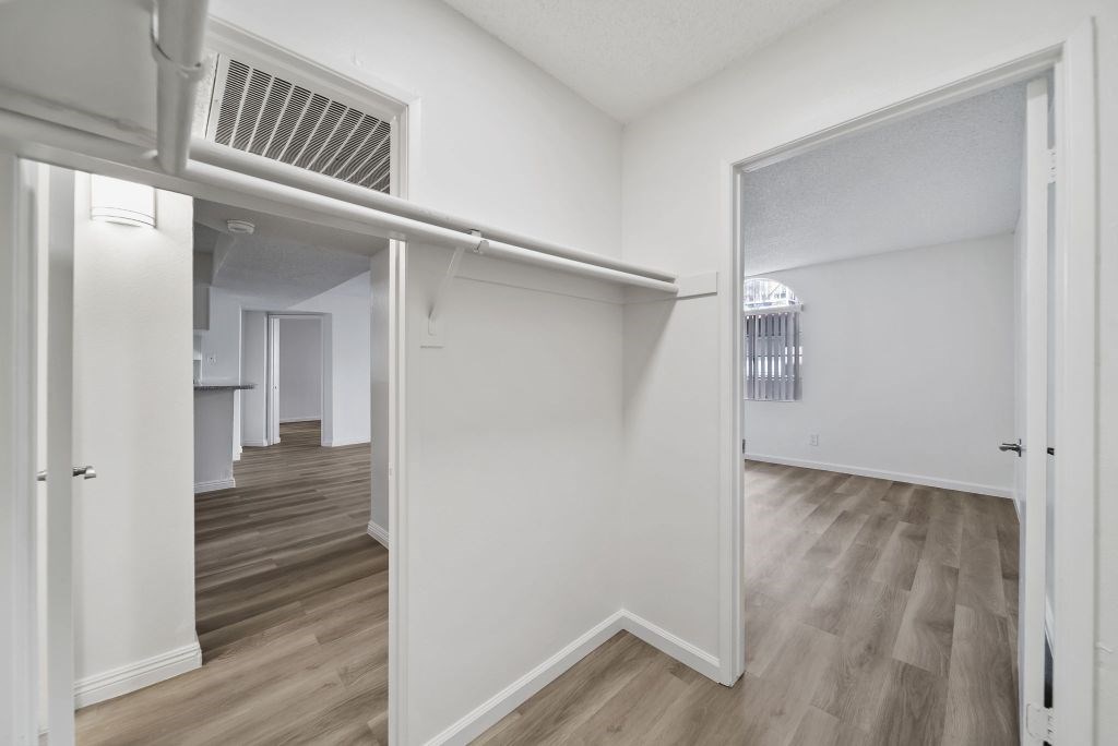 A room with white walls and wooden flooring with a doorway leading to another room.