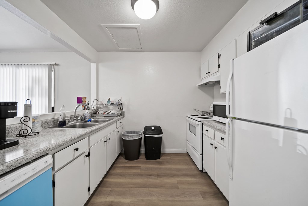 A kitchen with white appliances and a black trash can.