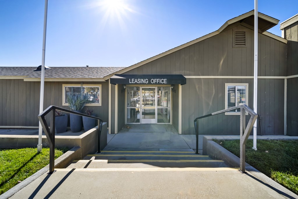 A leasing office building entrance with a bench and a sunny day.