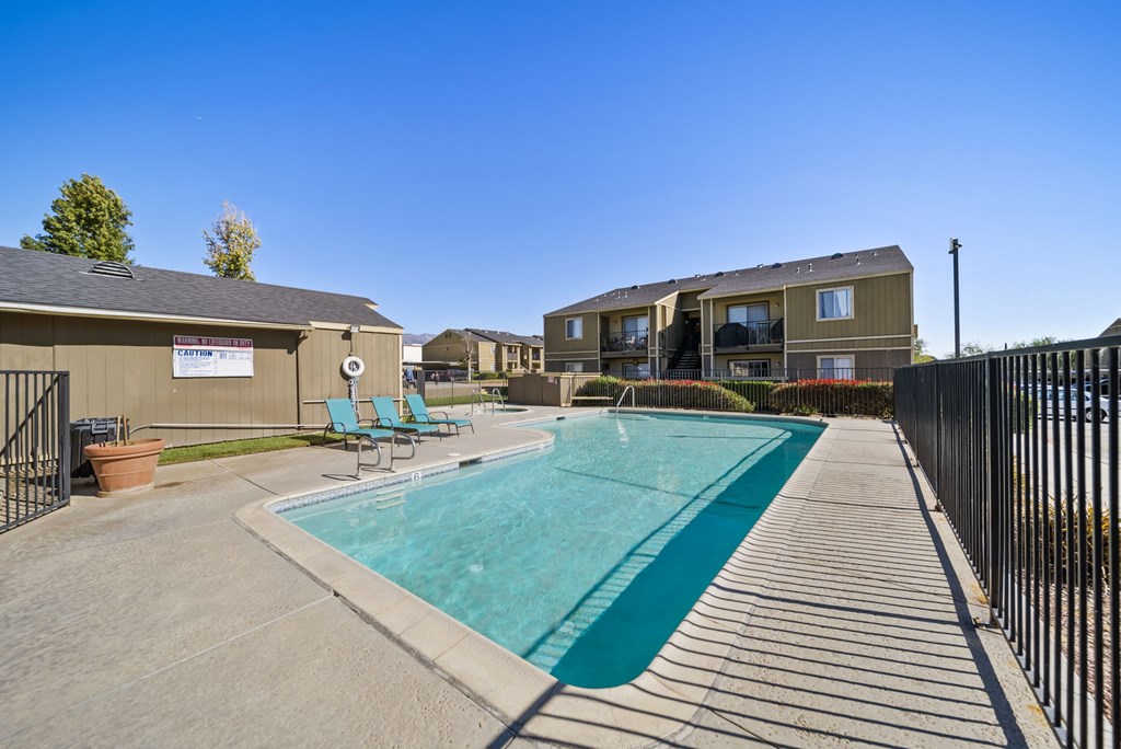 A swimming pool surrounded by a concrete walkway and a black fence.