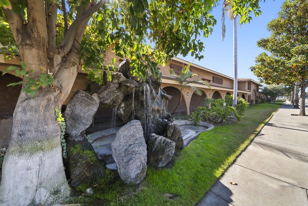 A small waterfall in a garden with a building in the background.