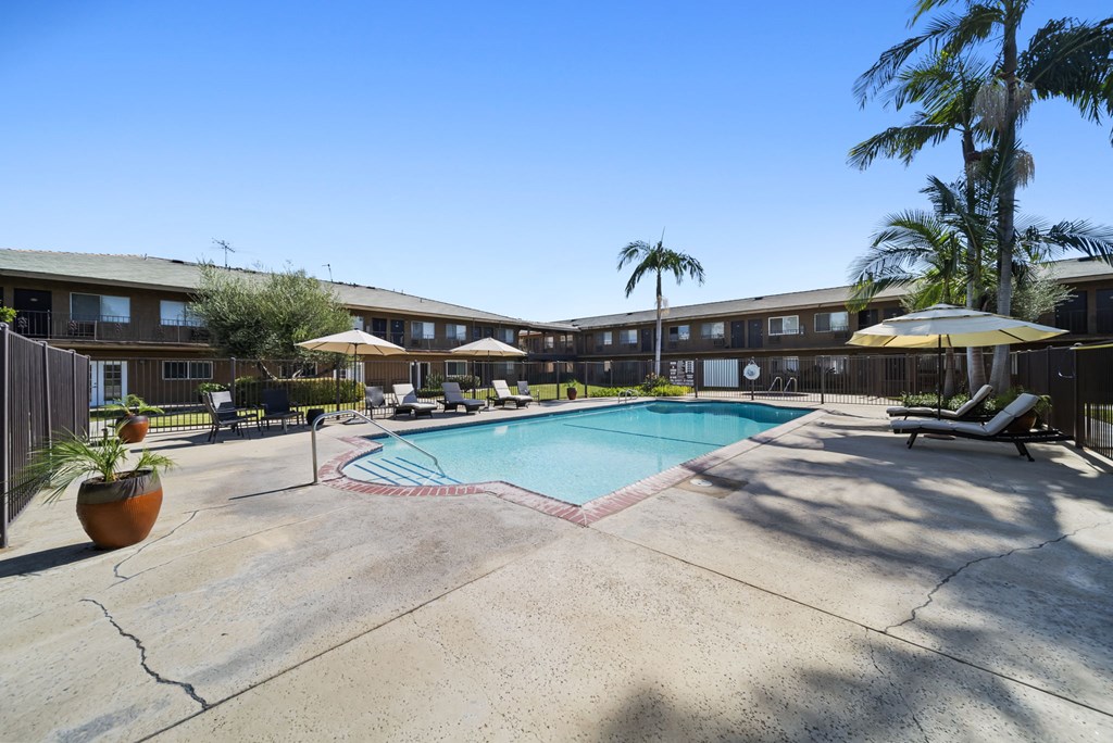 A pool surrounded by lounge chairs and umbrellas in front of a building.