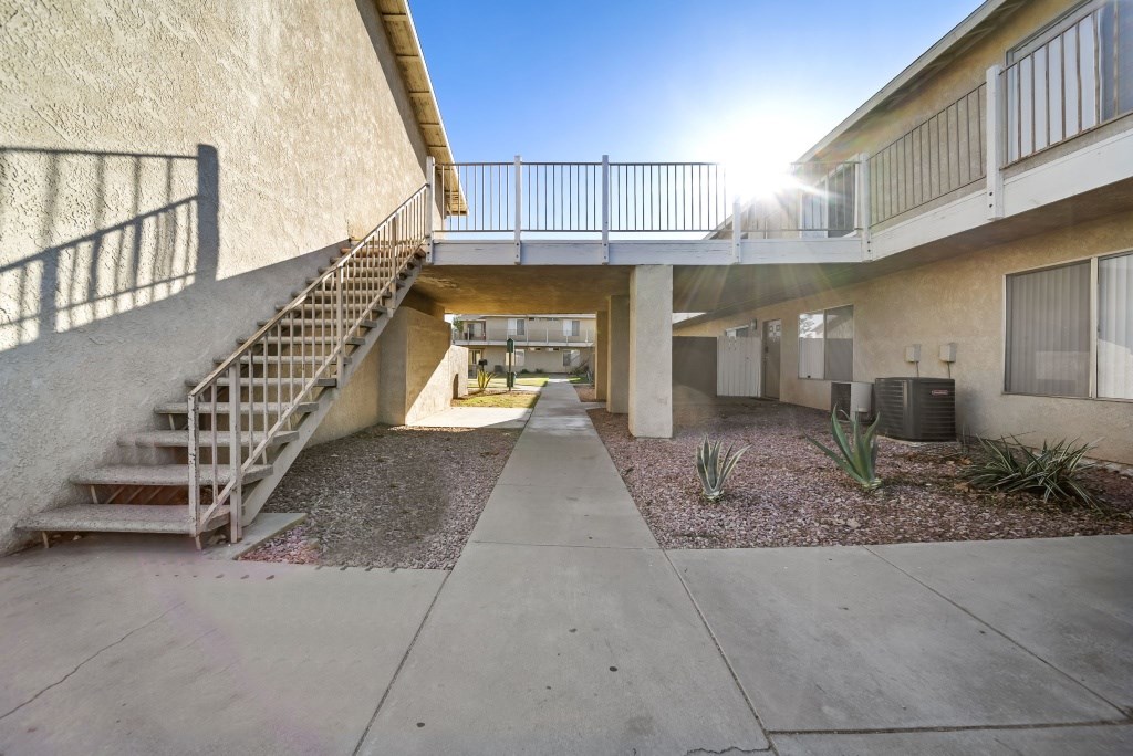 A sunny day at a courtyard with a staircase leading to a balcony.
