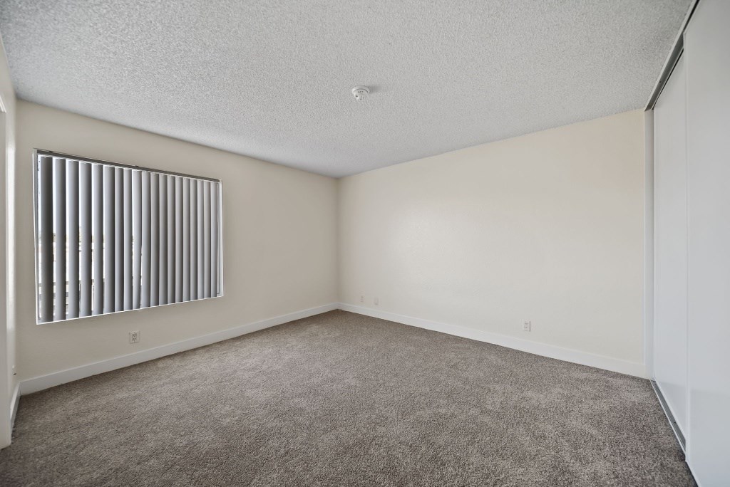 A room with a carpeted floor and a window with vertical blinds.