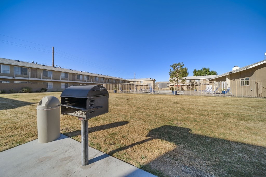 A mailbox sits on a concrete slab in front of a grassy area with apartment buildings in the background.