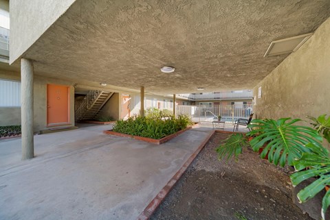 A concrete building with a red door and plants on the side.
