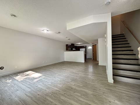 A spacious room with wooden flooring and a staircase on the right side.