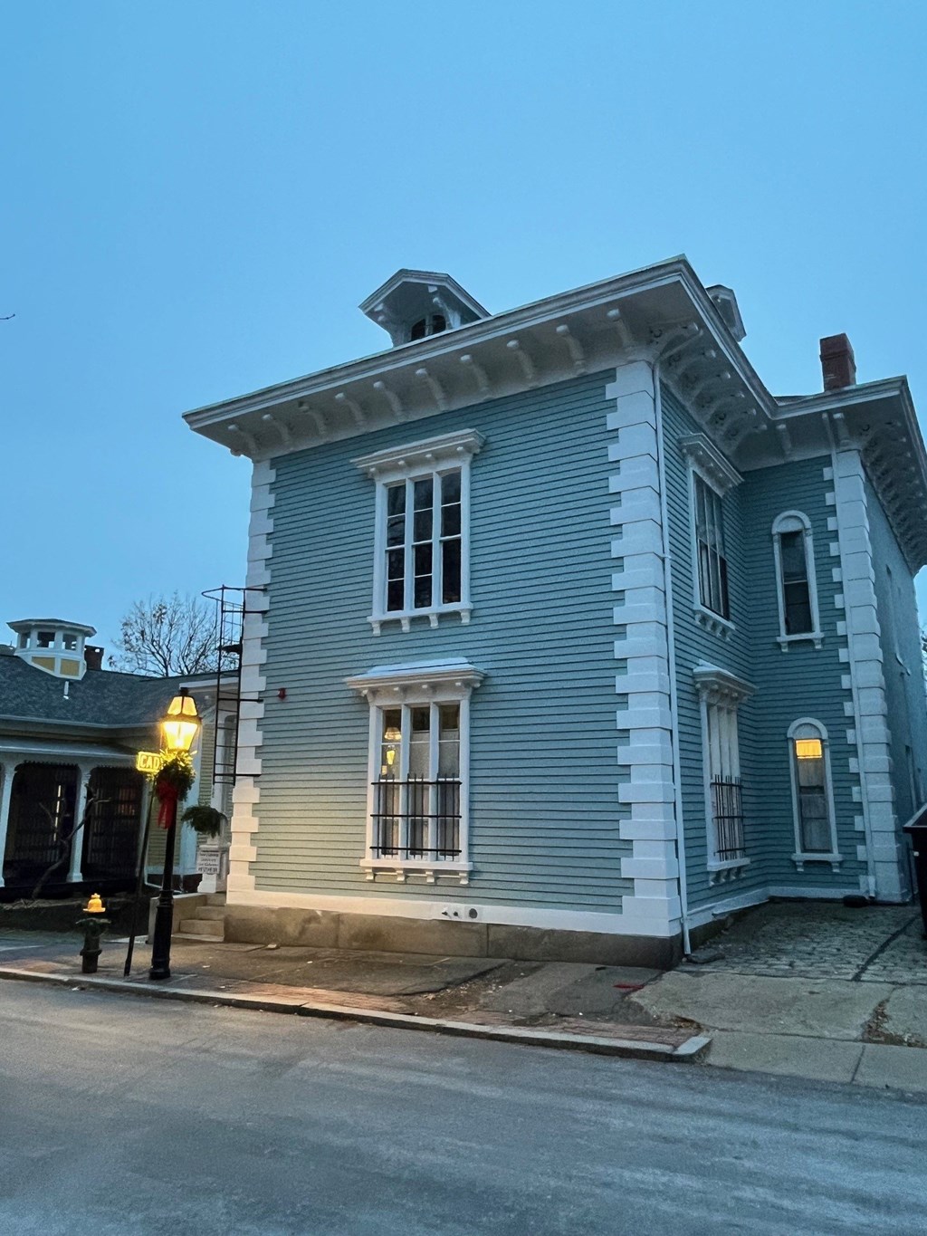 A blue house with white trim and a black iron railing on the porch.
