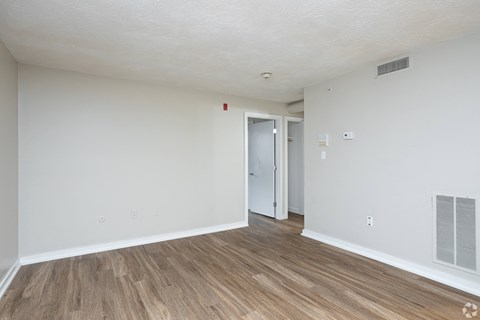 the living room of an apartment with white walls and wood flooring