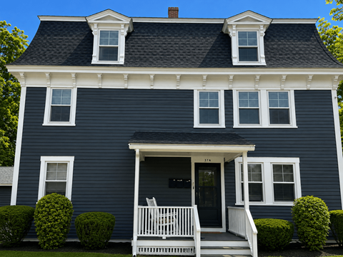 A blue house with a white porch and two windows on the roof.