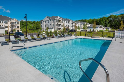 A swimming pool surrounded by lounge chairs and apartment buildings in the background.