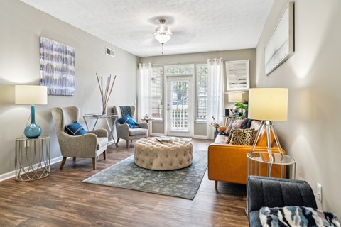A living room with a grey rug and a brown ottoman.