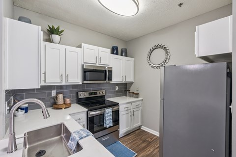 A kitchen with white cabinets and a grey refrigerator.
