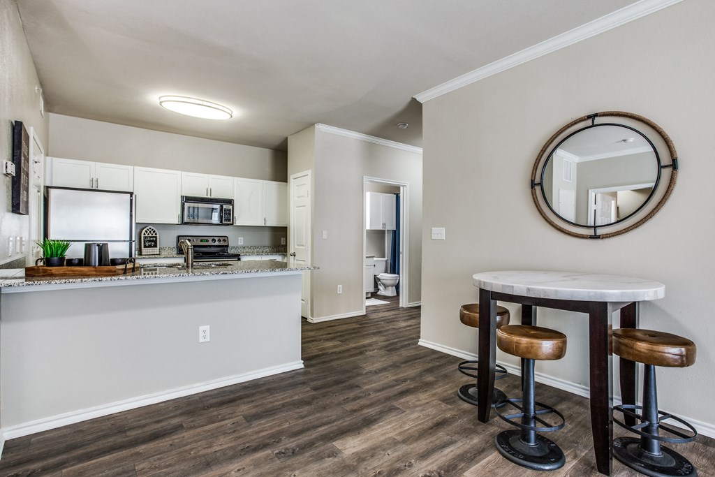 a living room with a kitchen and a bar with stools at Village of Hawks Creek Apartments, Westworth Village, TX 76114