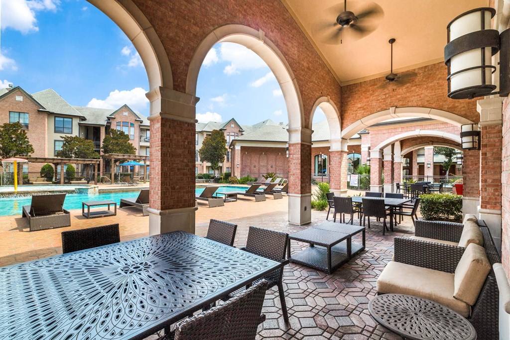 Patio with tables and chairs and a pool in the background at Vintage Park Apartments, Texas 77070