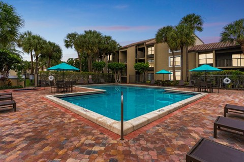 A pool surrounded by a brick patio and palm trees. A pool surrounded by a brick patio and palm trees at Boca Colony Apartments, Boca Raton, FL