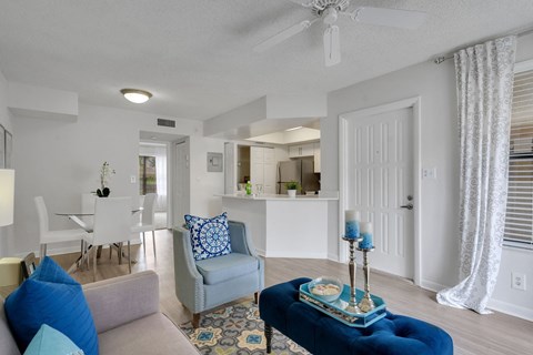 A living room with a grey couch, a blue ottoman, and a white ceiling fan at Boca Colony Apartments, Boca Raton, FL