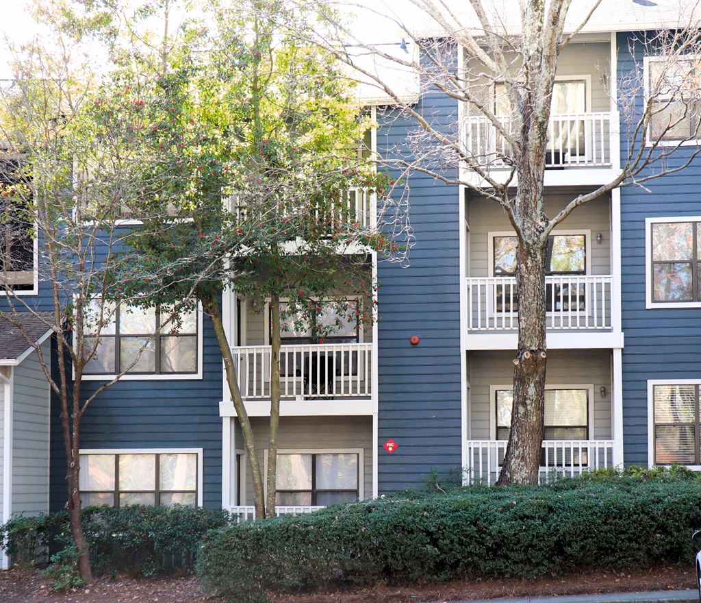 the exterior of a blue apartment building with trees and shrubs