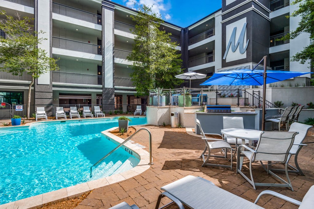 A pool area with chairs and a building in the background. at Montecito Apartments, Houston, TX, 77056