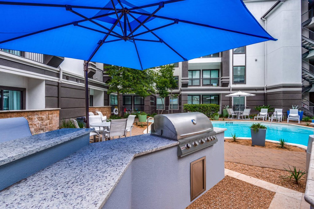 A blue umbrella shades a table and chairs on a patio. at Montecito Apartments, Houston, TX