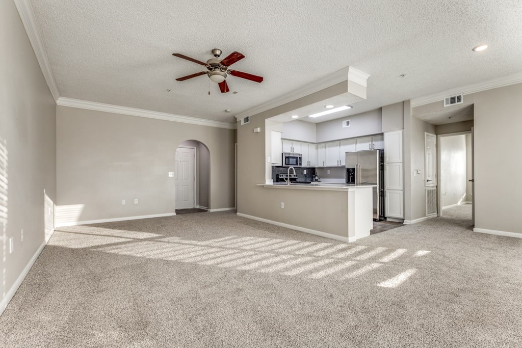 A spacious living room with a ceiling fan and a kitchen area in the background. at Montecito Apartments, Houston, Texas
