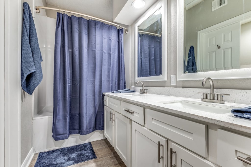 A bathroom with a white vanity and a blue shower curtain. at Montecito Apartments, Houston, TX