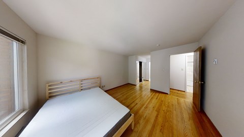 A bedroom with a bed, wooden floors, and a window with blinds.