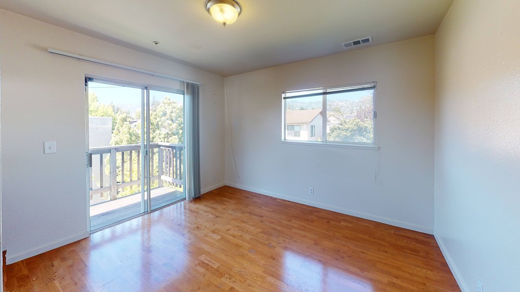 A room with wooden floors and a sliding glass door leading to a balcony.