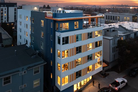 A tall building with a blue and white facade stands in the foreground of a cityscape at dusk.