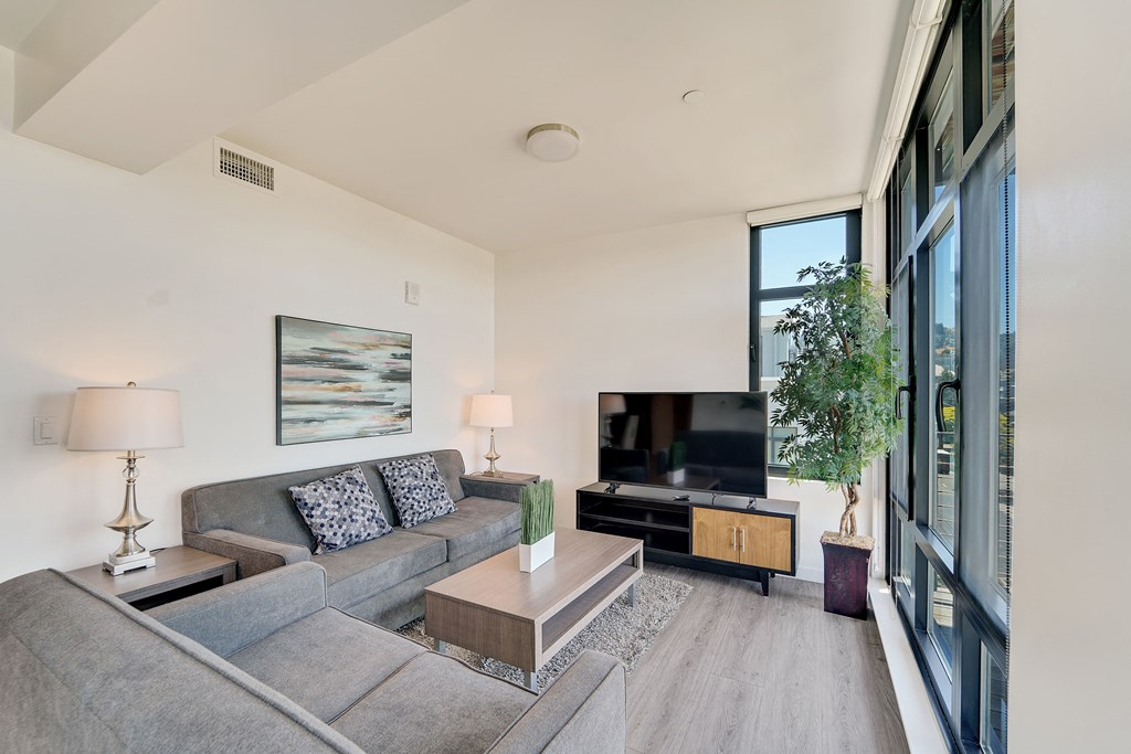 A living room with a grey couch and a painting on the wall.