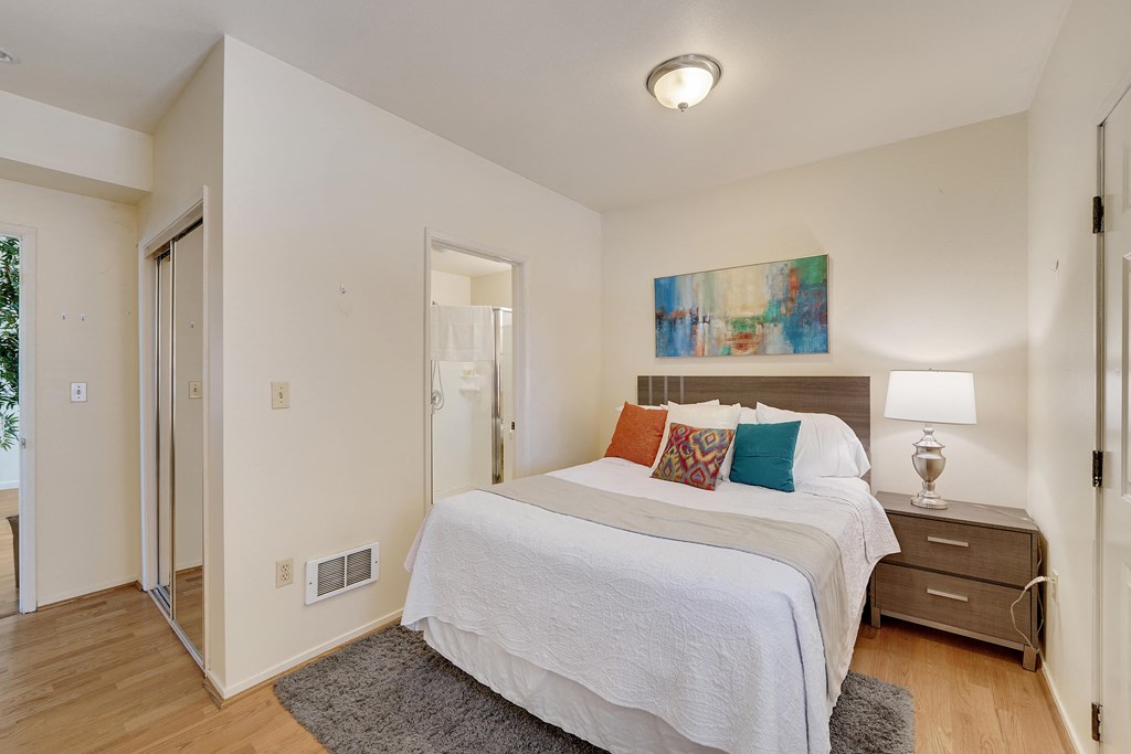 A bedroom with a white bed and a painting on the wall.