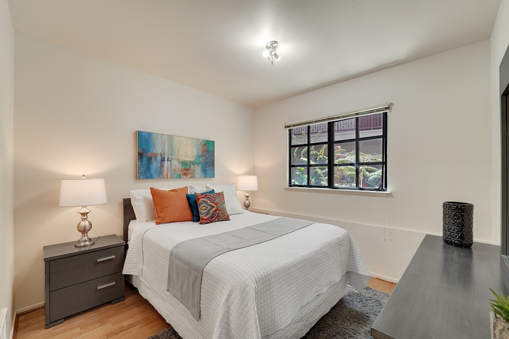 A bedroom with a bed, nightstand, and a painting on the wall.