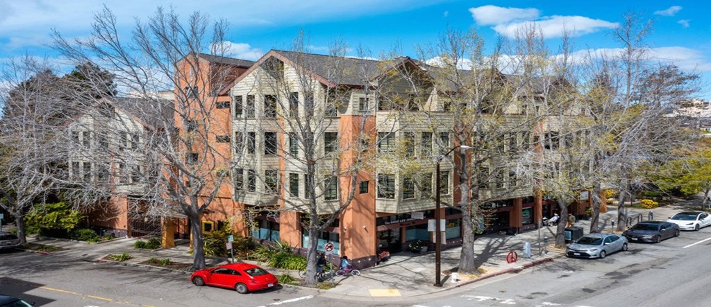 A red car is parked on the street in front of a large building.