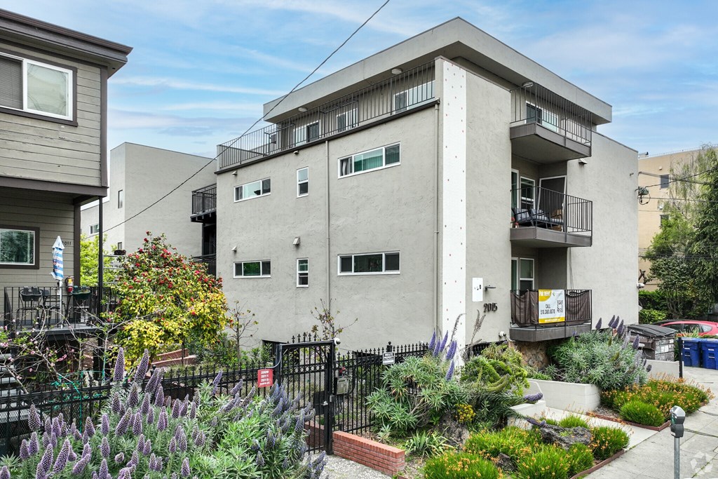 A grey building with a balcony and a small garden in front.