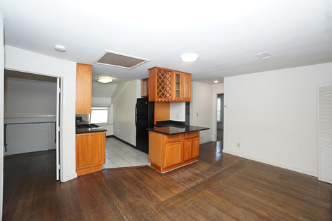 an empty living room and kitchen with wood flooring and a black counter top