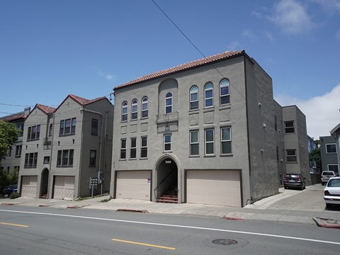 A grey building with a red tile roof is situated on a street corner.